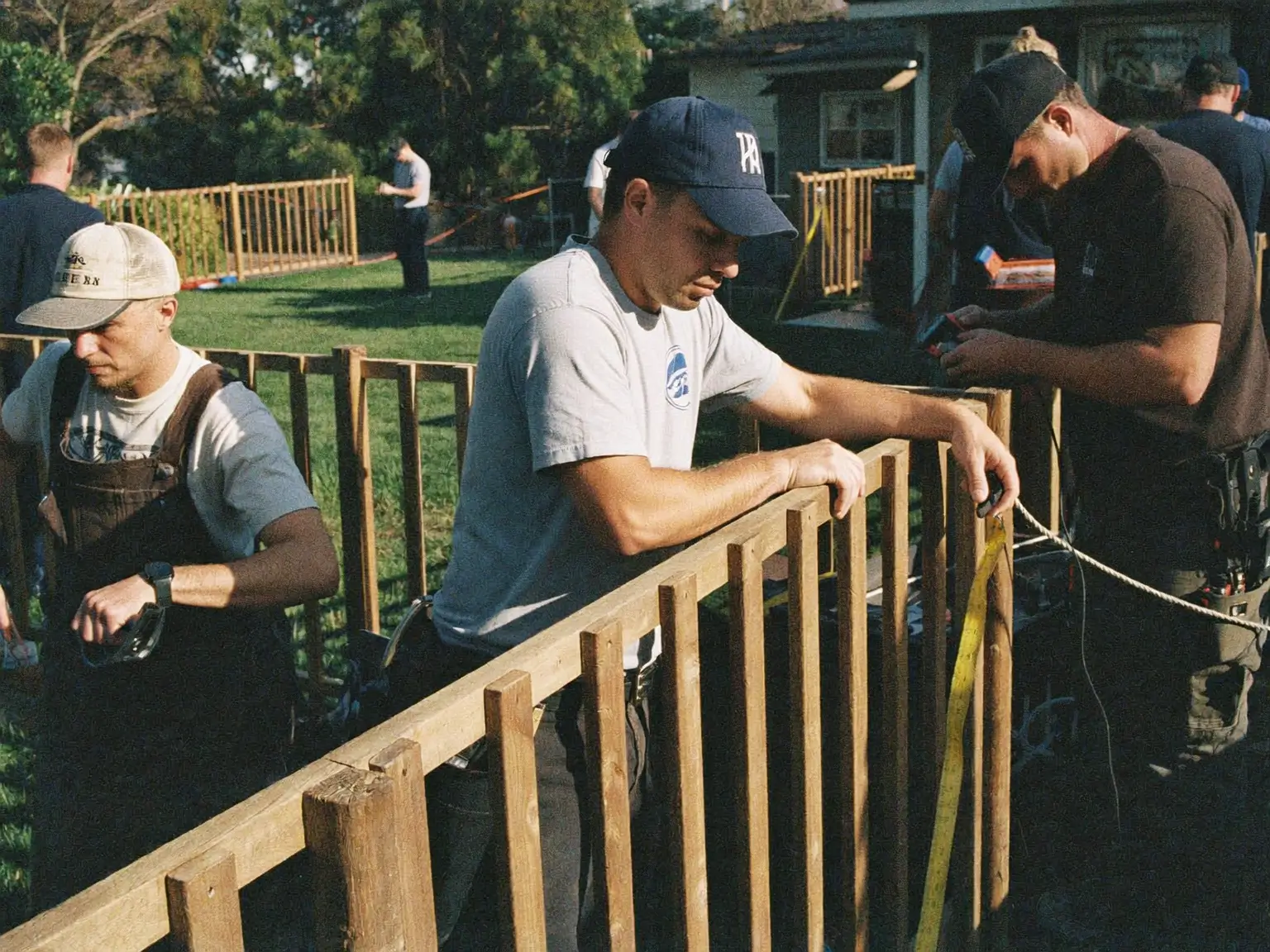 B.C. Fence crew setting cedar pickets on a backyard fence line, one running a tape measure along the rail